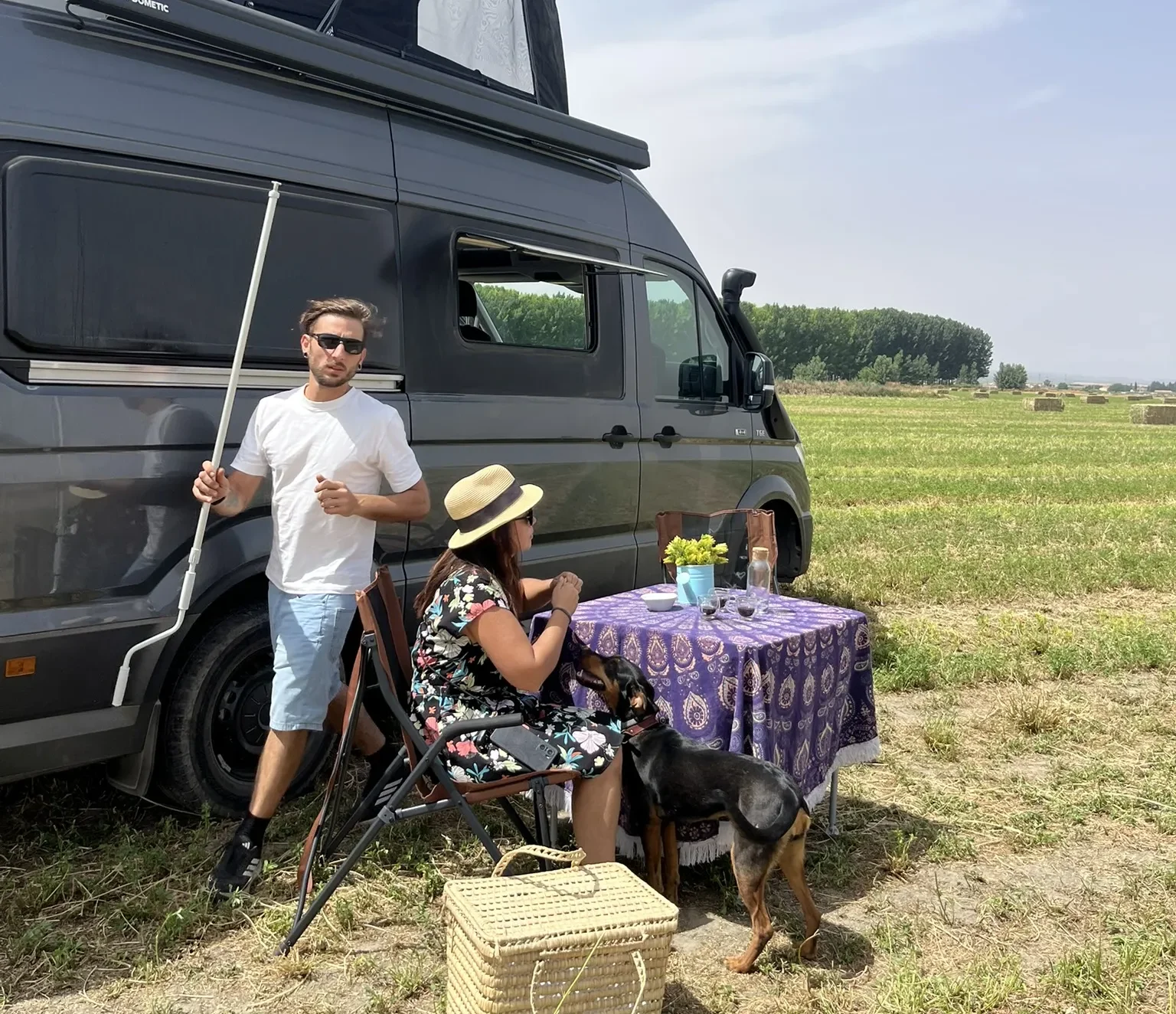 Pareja con perro montando campamento junto a furgoneta camper MAN TGE abriendo toldo Dometic con luces
