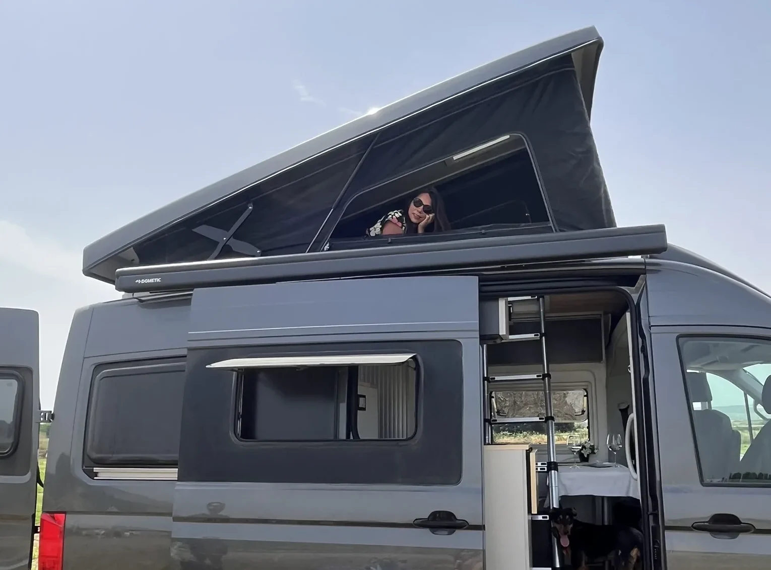 Chica acostada asomando la cabeza desde el techo elevable de furgoneta camper MAN TGE